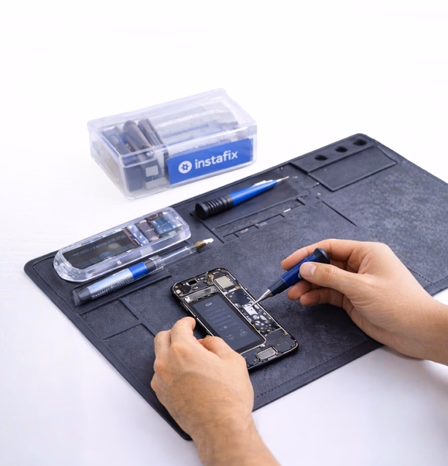 Technician working on an opened phone with a screwdriver on a repair mat, an Instafix parts case beside it